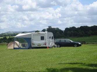 A caravan with an awning and a car on the grass campsite