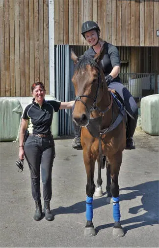 Two members of the team in the yard with a bay horse wearing boots
